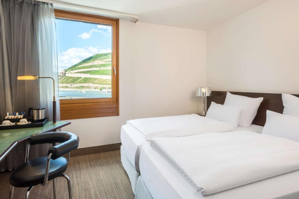 莱茵河畔的宾根宾根NH酒店的酒店客房设有两张床、一张书桌和一个窗户。