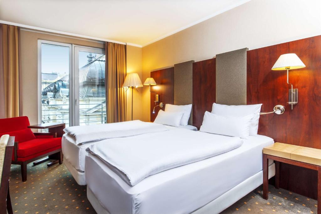 布达佩斯NH布达佩斯市酒店的酒店客房,设有两张床和一张红色椅子