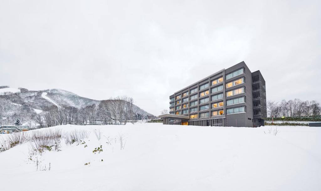 二世古Hinode Hills Niseko Village - Small Luxury Hotels of The World的田野前雪地中的建筑物