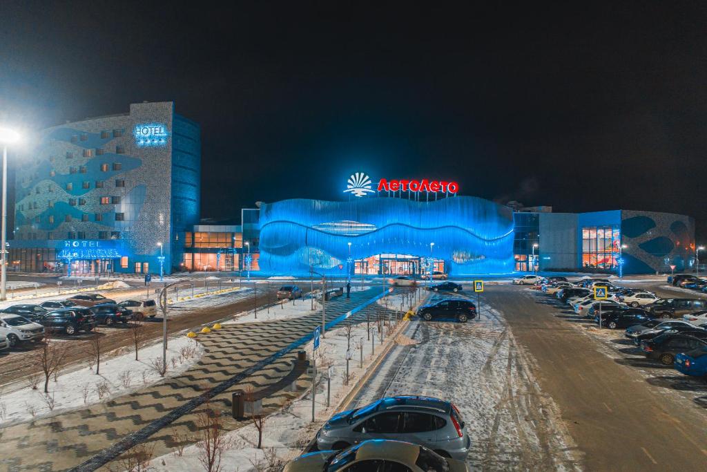 秋明ЛетоЛето Термал Резорт & СПА的一座蓝色的大建筑,汽车停在停车场