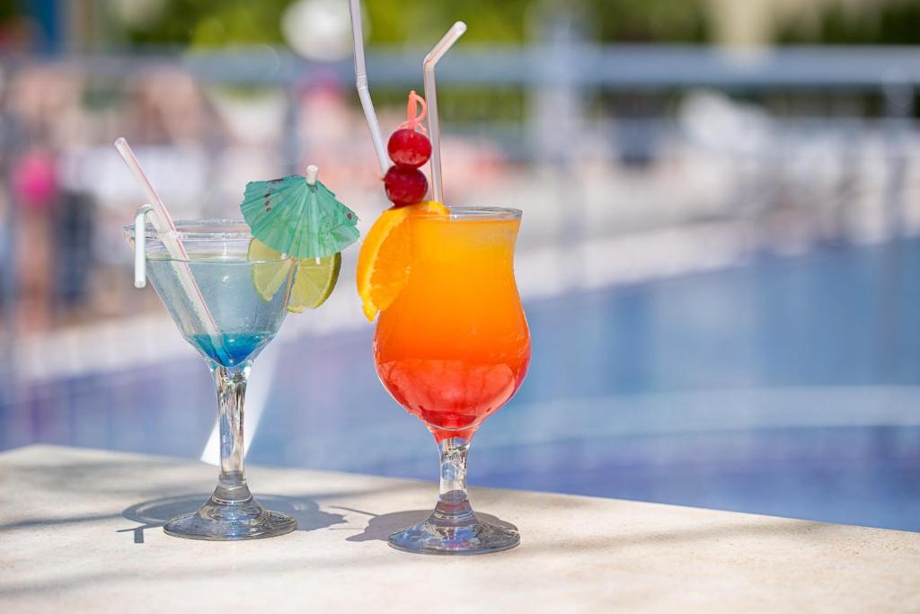 普里莫尔斯科Perla Sun Beach Hotel - All Inclusive的坐在泳池旁的桌子上,喝上两杯鸡尾酒
