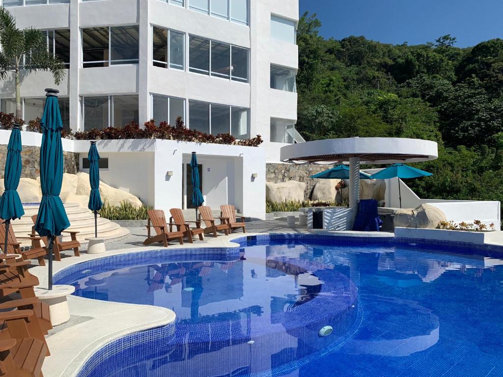 阿卡普尔科La Villa de Almudena的一座带椅子和遮阳伞的游泳池位于一座建筑旁边