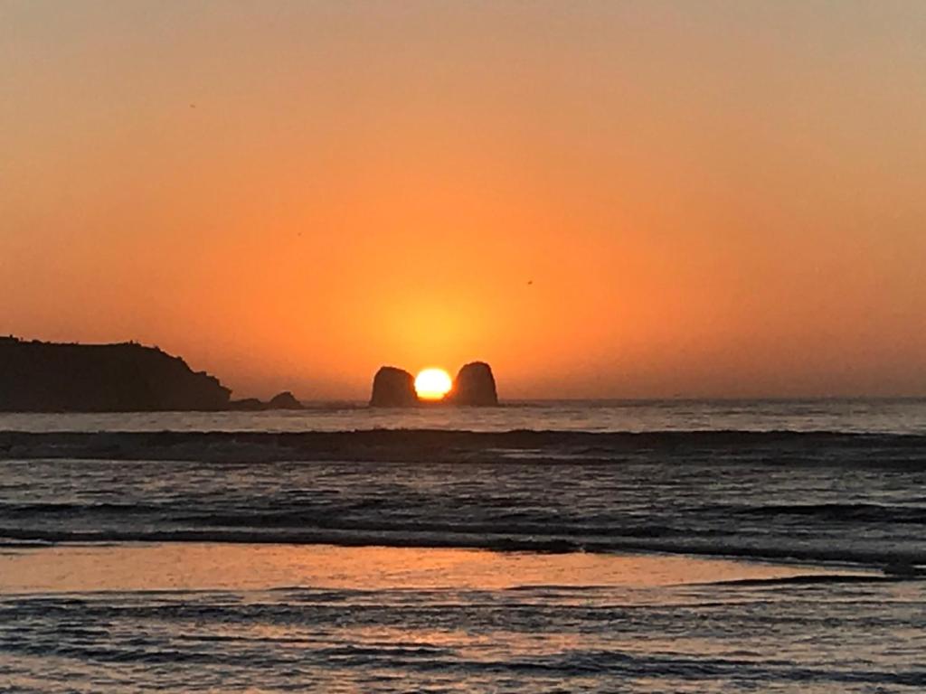 皮奇勒姆Esfera Pichilemu - Lodge的海洋上的日落,有两个大的岩石层