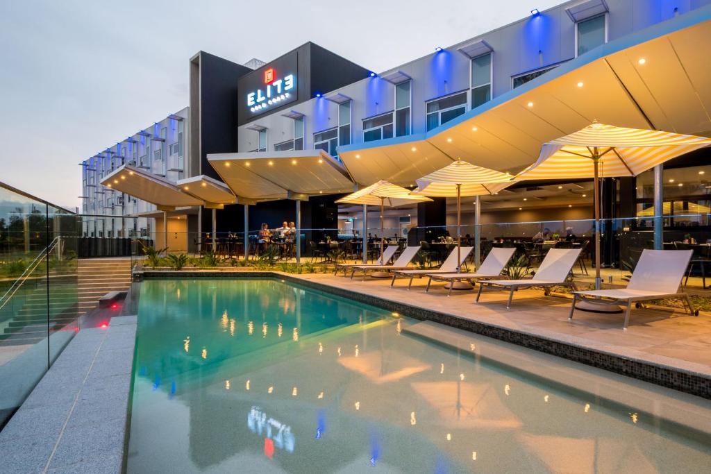 黄金海岸Elite Gold Coast的酒店大楼前的游泳池配有椅子和遮阳伞