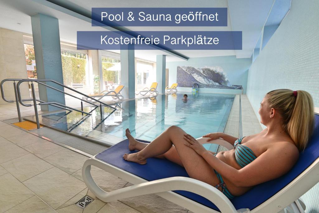 雷根斯堡Hotel Apollo Garni的坐在游泳池椅子上的穿着泳衣的女人