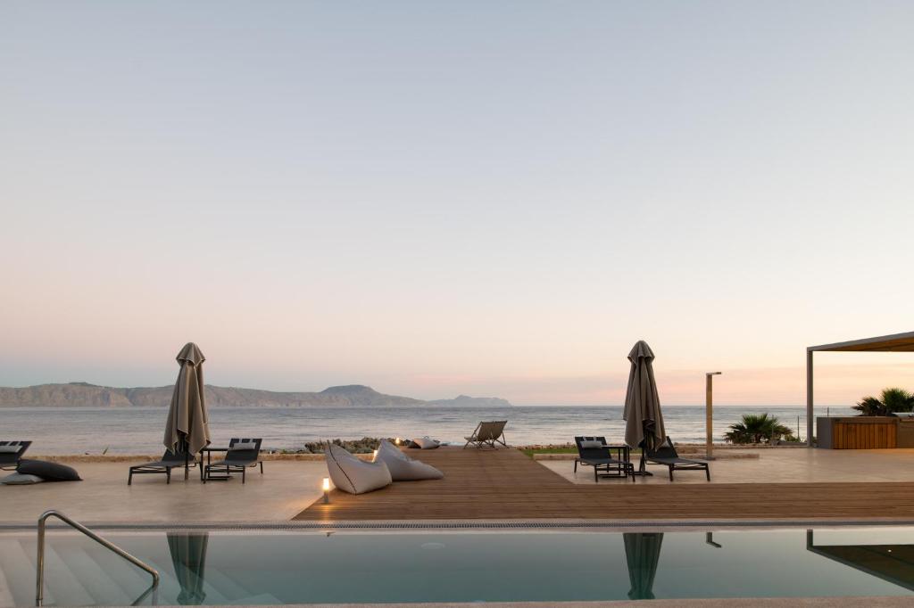 PetresAn intimate Villa Resort- Right on the beach, by ThinkVilla的毗邻大海的带椅子和遮阳伞的游泳池