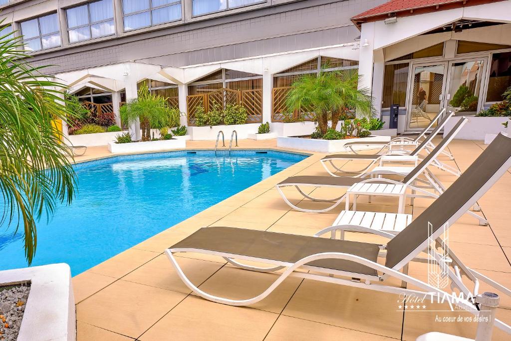 阿比让Hotel Tiama Abidjan的大楼前带躺椅的游泳池