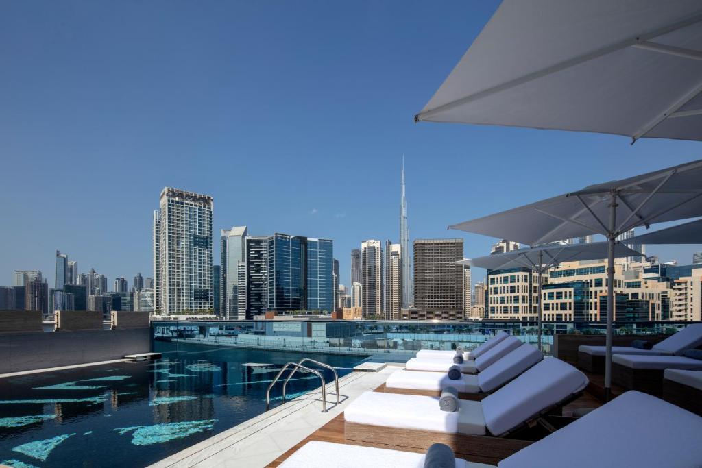 迪拜Hyde Hotel Dubai的一个带白色躺椅的游泳池,享有城市天际线