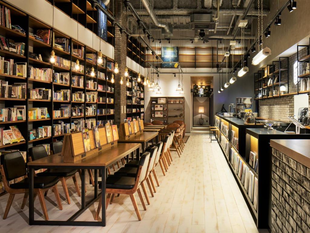 福冈LAMP LIGHT BOOKS HOTEL fukuoka的一间设有桌椅的餐厅,位于带书架的房间