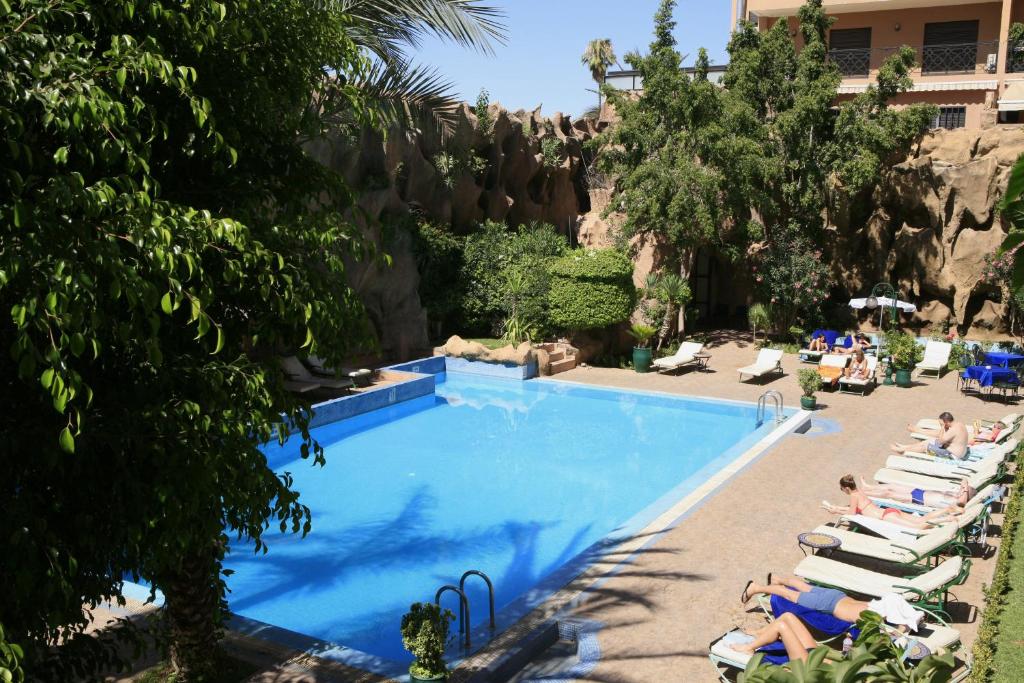 马拉喀什帝豪假日Spa酒店的一个带躺椅的游泳池,度假村内有工作人员