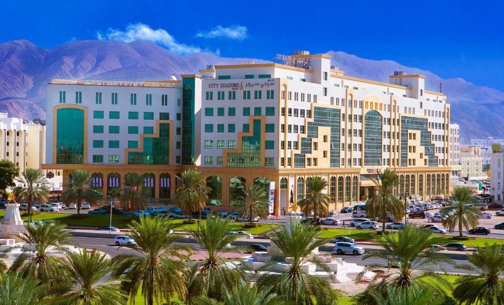 马斯喀特City Seasons Hotel & Suites Muscat的停车场内棕榈树的大型建筑