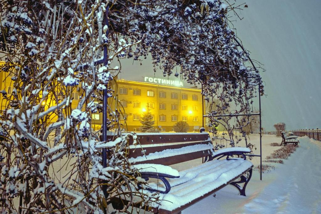 VotkinskZhemchuzhina Hotel的黄色建筑前的雪盖长椅