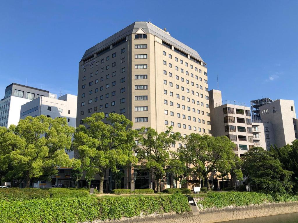 广岛HOTEL MYSTAYS Hiroshima Peace Park的一座高大的白色建筑,前面有树木