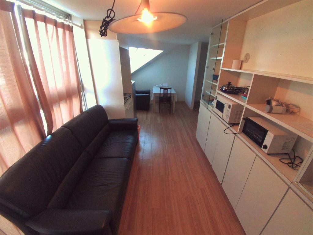 东京Palette Takashimadaira guest house的一间带黑色沙发的客厅和一间厨房