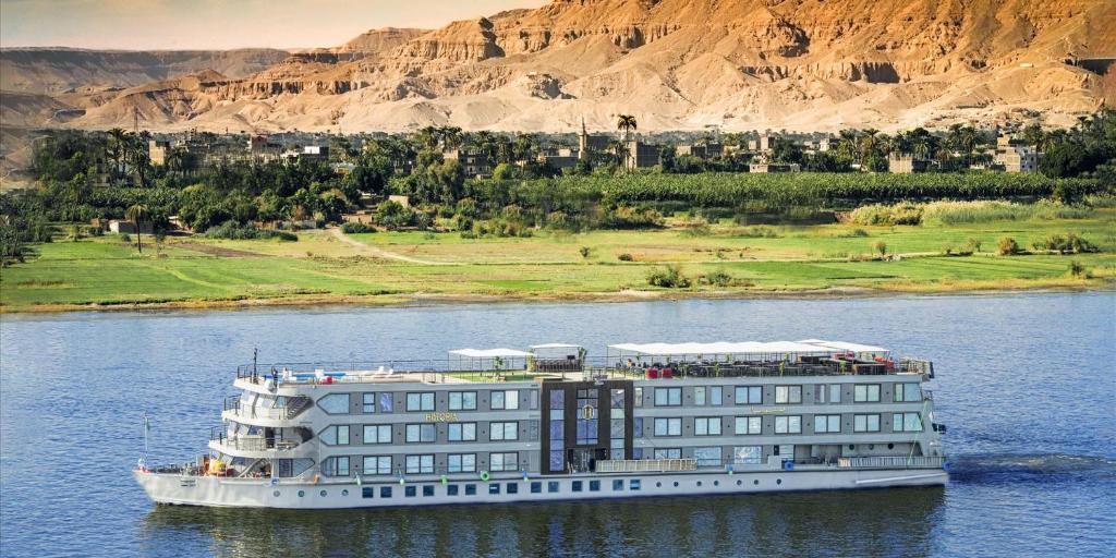 卢克索Historia The Boutique Hotel Nile Cruise - Every Monday from Luxor for 04 & 07 Nights - Every Friday From Aswan for 03 & 07 Nights的建筑物旁边的水面上的游轮