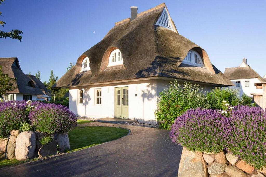 富伦多夫Holiday house, Fuhlendorf的茅草屋顶的房子,前面有紫色的花