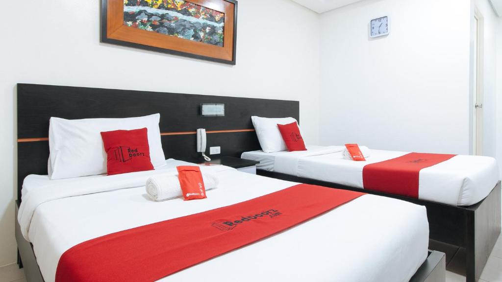 马斯巴特RedDoorz @ Greenview Hotel and Restobar Masbate的两张位于酒店客房的床,配有红色和白色枕头