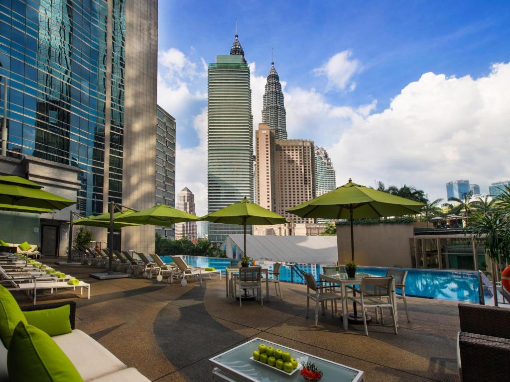 吉隆坡吉隆坡宴宾雅酒店的一个带桌子和遮阳伞的屋顶露台,享有城市天际线
