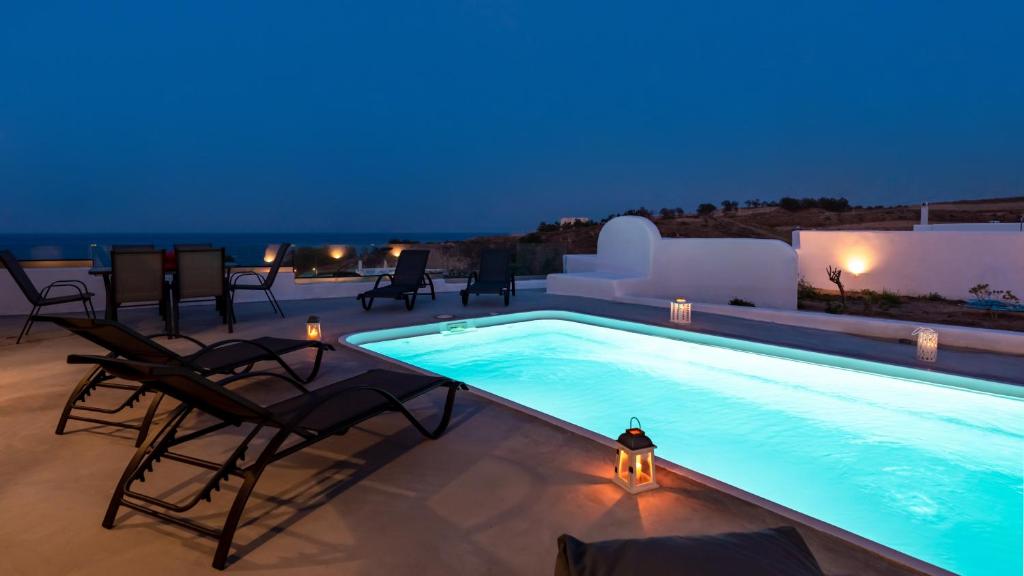 莫诺利索斯Villa Waves的夜间游泳池,配有椅子和桌子