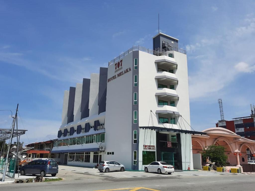 马六甲707 Hotel (Cheng Ho ) Melaka的白色的建筑,有汽车停在停车场