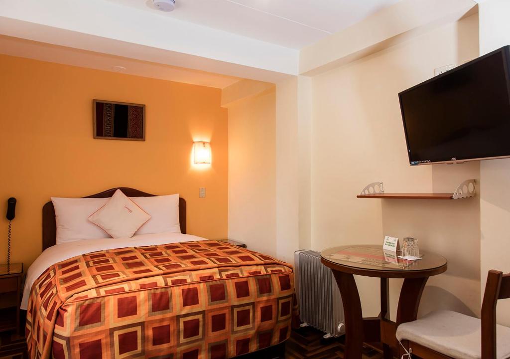库斯科Laramani Hotel Boutique的一间酒店客房,配有一张床铺、一张桌子和一台电视
