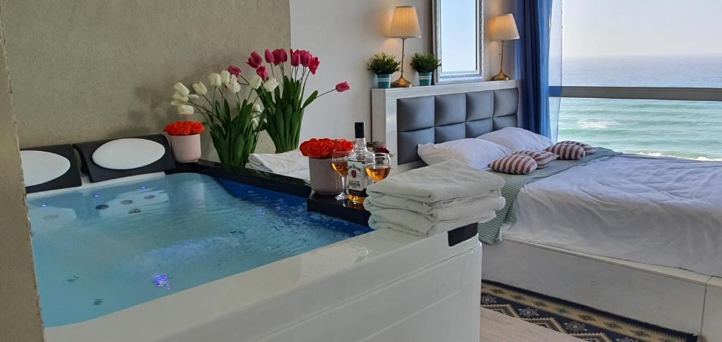 内坦亚Royal suite with sea view- private jaccuzi-Also suitable for orthodox people的一间带浴缸、一张床和鲜花的卧室