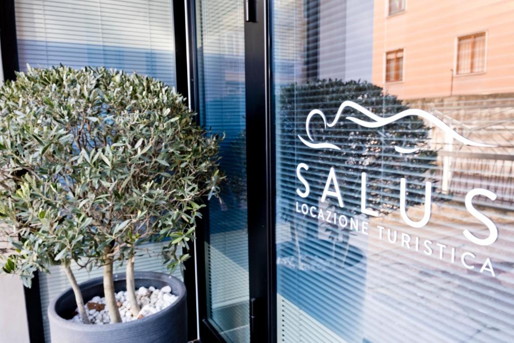 维罗纳SALUS Locazione Turistica的商店橱窗上的标志,有盆栽的树