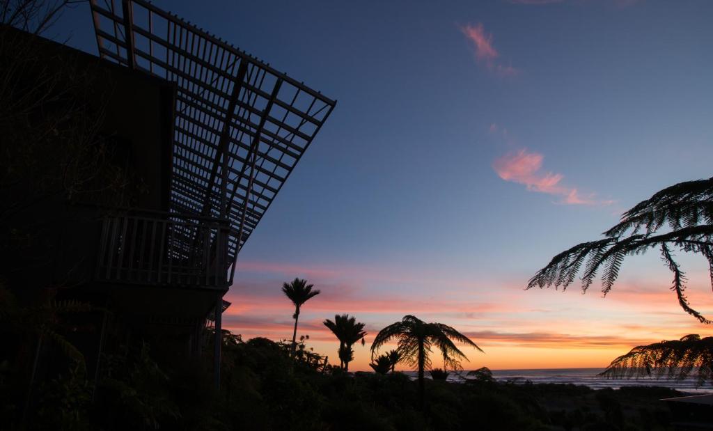 普纳凯基Scenic Hotel Punakaiki的棕榈树海滩和一座建筑的日落