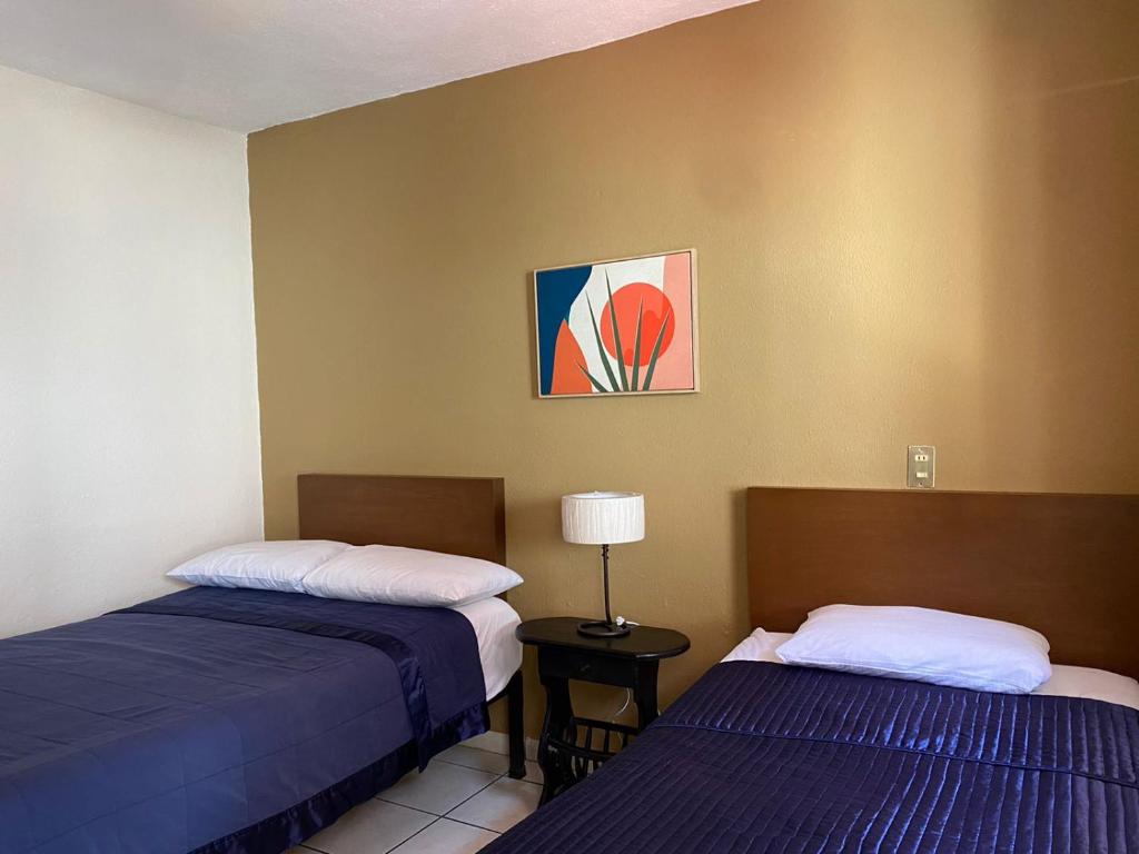 科利马Hotel Caracoles Colima的客房设有两张床和一张带台灯的桌子。