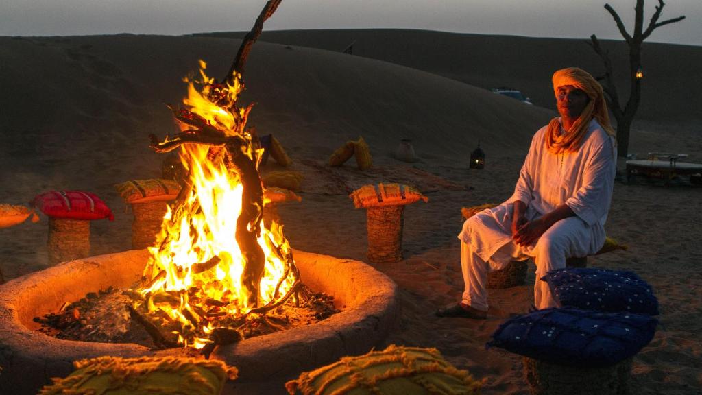 El GoueraAtta Desert Camp的坐在沙漠火坑旁的女人