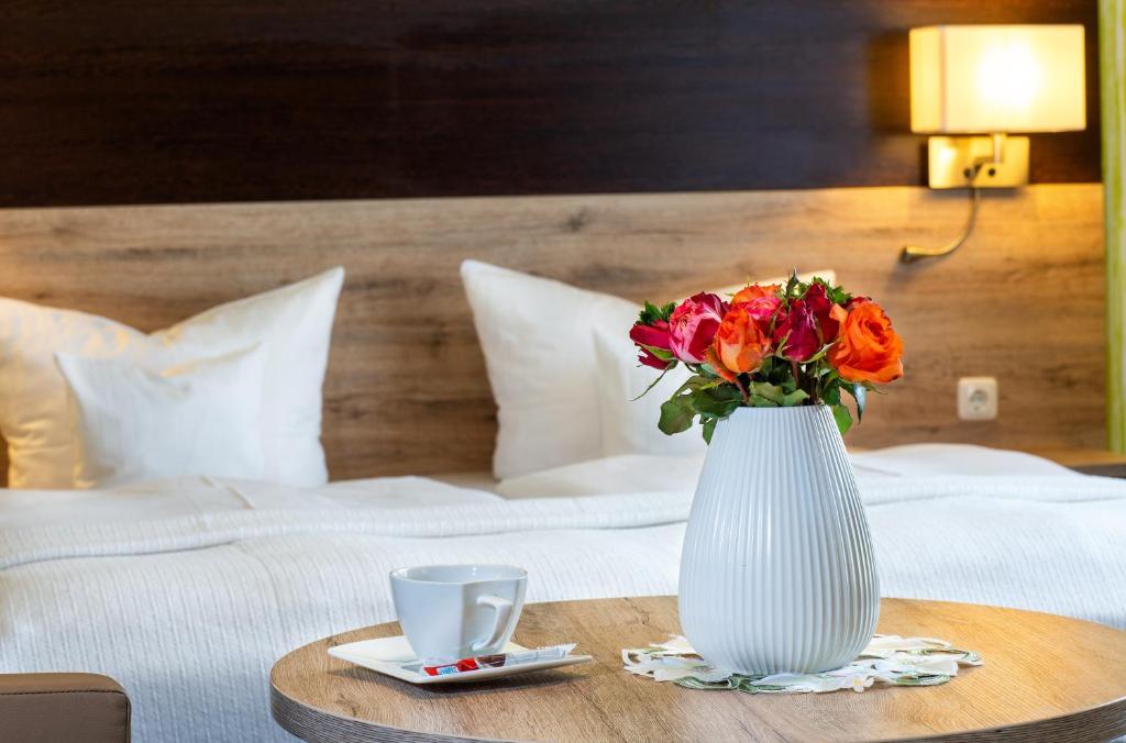 罗斯多夫Appart Hotel Roßdorf的一张白色花瓶,在床边的桌子上放着鲜花