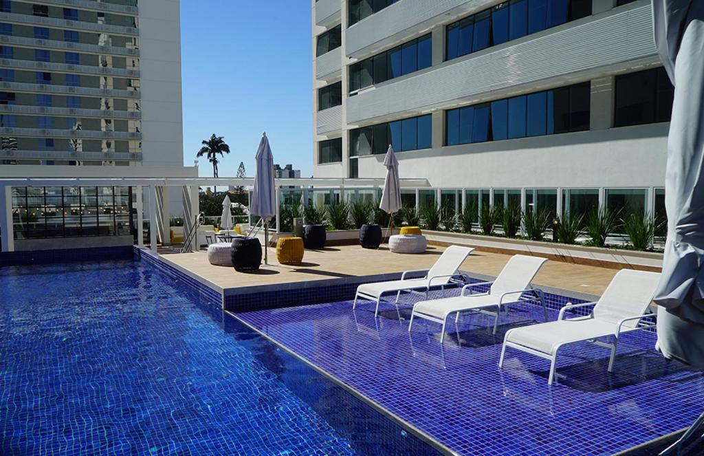坎普斯戈伊塔卡济斯Apart Hotel - América Residence Campos dos Goytacazes的一座带白色椅子的游泳池和一座建筑