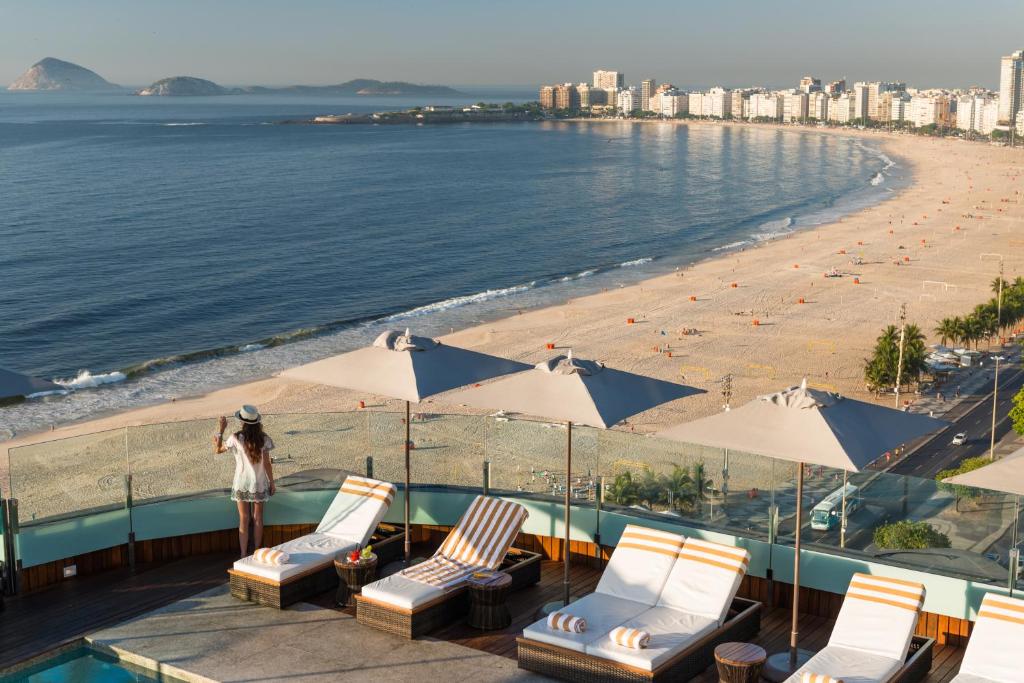 里约热内卢里约热内卢波尔图湾酒店的一名妇女站在海滩旁,带椅子和遮阳伞