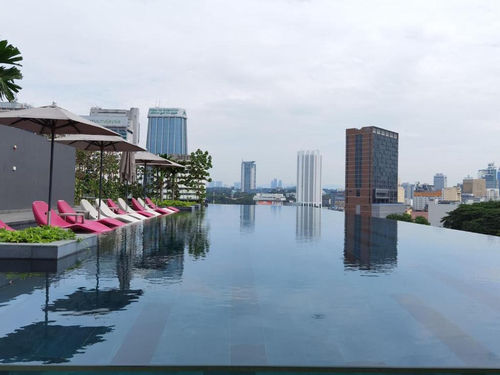 吉隆坡OPUS RESIDENCE KL I HomeBrickz的一座大楼内的游泳池,配有椅子和遮阳伞