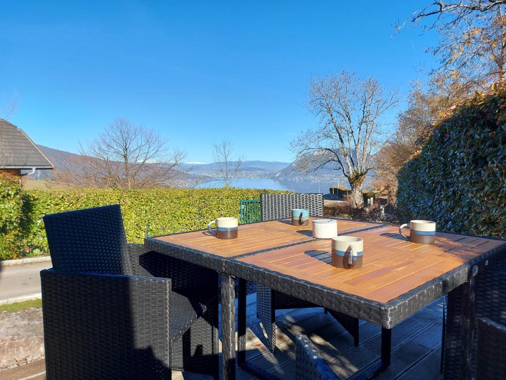 圣若里奥Entre lac et montagne, chaleureuse maison 3 pièces avec très belle vue lac d'Annecy. Terrasse, jardin, parking, cheminée, barbecue ….的一张木桌,上面有杯子