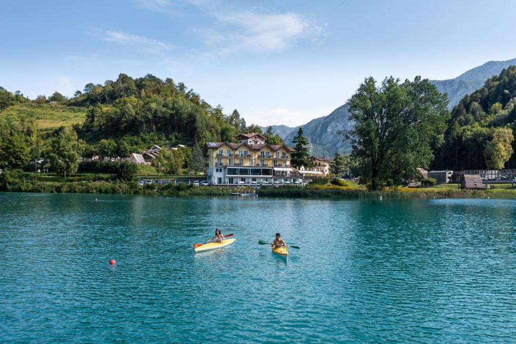 莱德罗Panoramic Hotel San Carlo Ledro的两人在房子前的湖上划皮艇