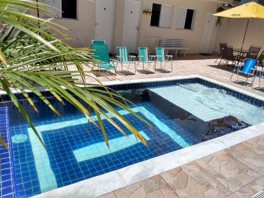 瓜鲁雅Suíte Sanlubia Enseada Guarujá的一个带棕榈树、椅子和桌子的游泳池