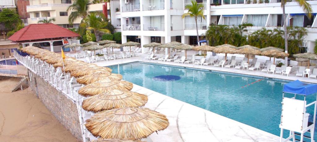 阿卡普尔科Suites Torres Gemelas VIP的大楼旁的游泳池配有稻草遮阳伞和椅子