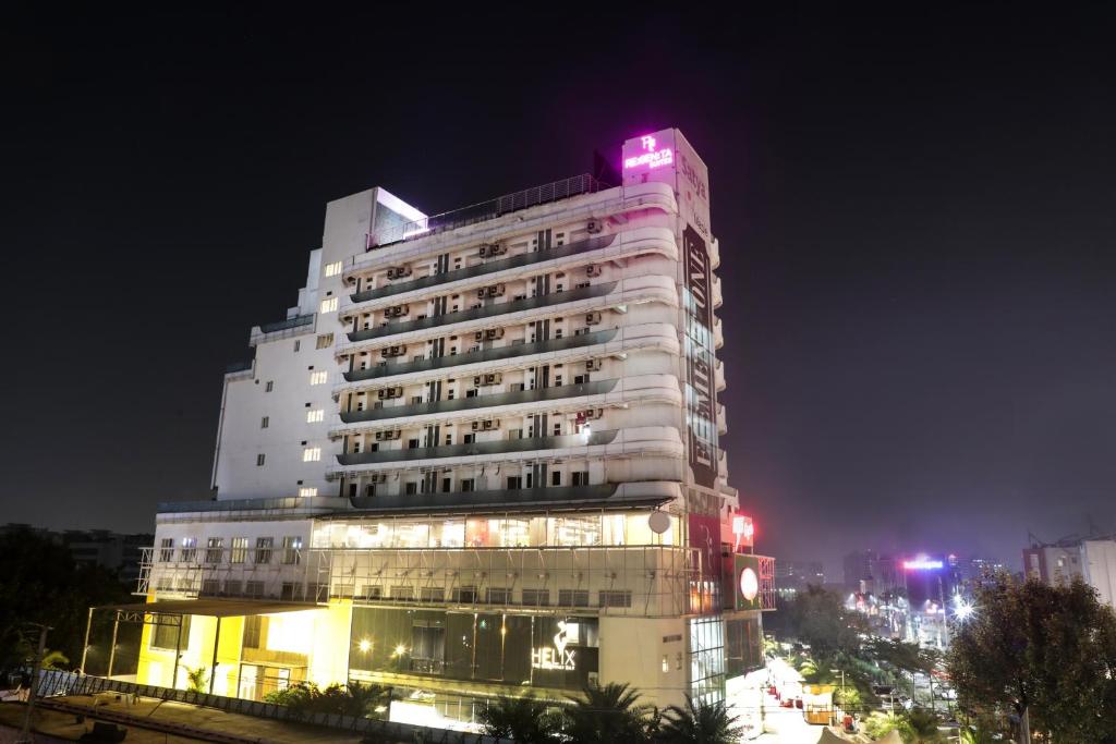 古尔冈Regenta Suites Gurugram, Sohna Road, Sector 49的一座高大的白色建筑,上面有粉红色的灯光