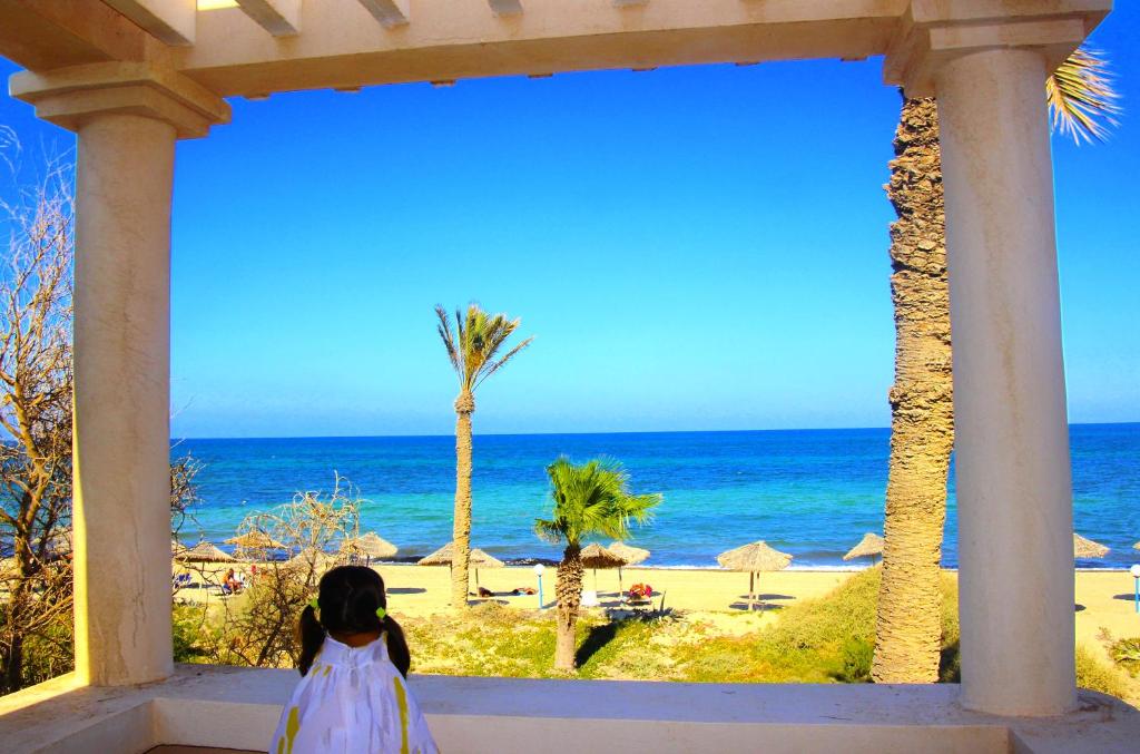 杰尔吉斯Zita Beach Resort的穿着白色衣服的小女孩,看着大海