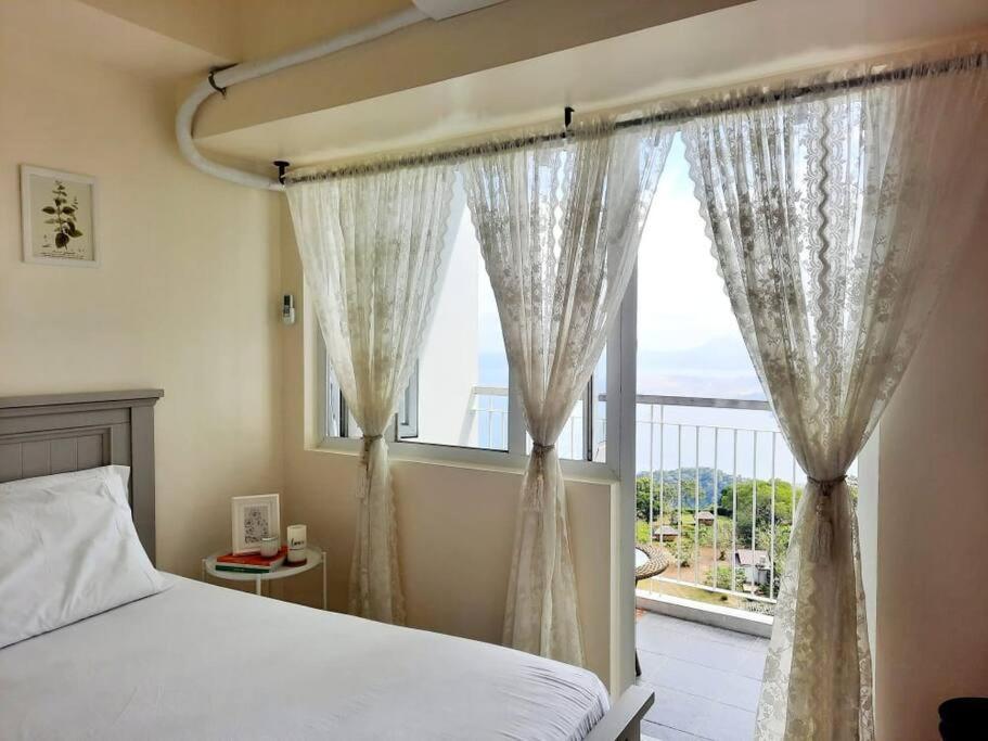 大雅台1 BR Cozy Farmhouse-Style Condo with Balcony & Taal View at Wind Residences的一间卧室设有一张床和一个大窗户