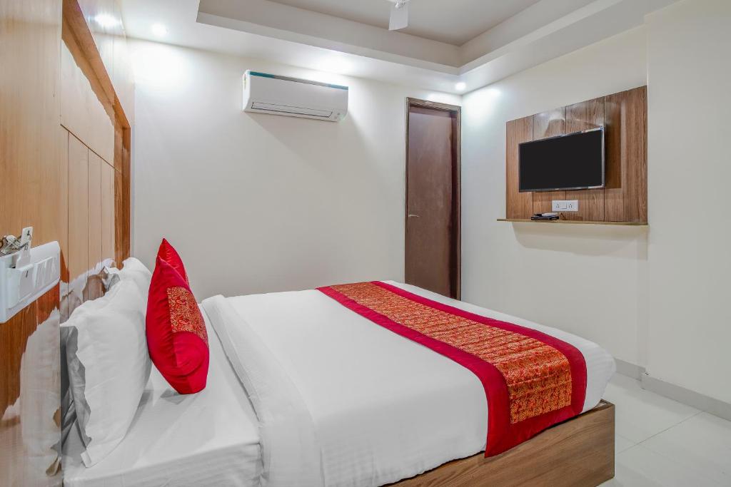 新德里Hotel Classic Paradise Inn的一间卧室配有一张带红色枕头的床和一台电视。