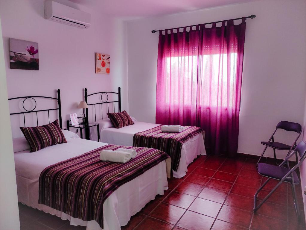 Villanueva del FresnoCasa Rural La Aduana的客房设有两张床和一个带粉红色窗帘的窗户。