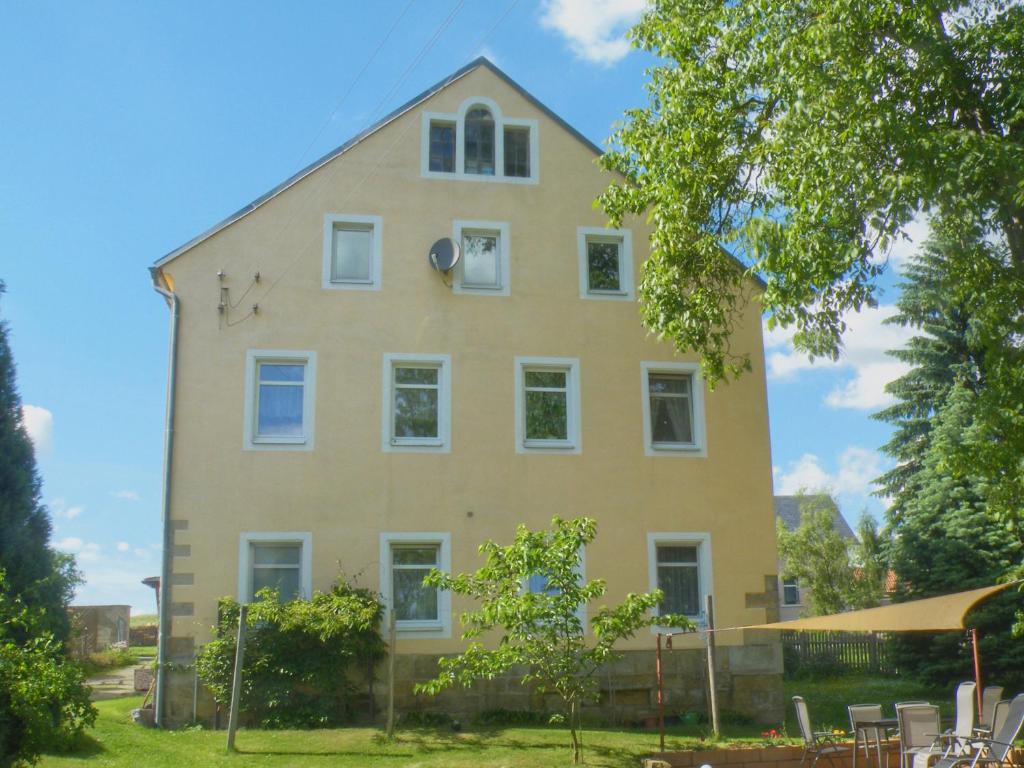 KirnitzschtalFerienwohnung Am Lindenbaum的一间黄色的大房子,有白色的窗户和树