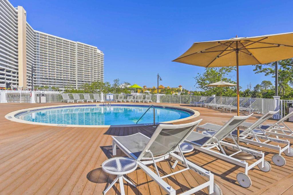 巴拿马城海滩Panama City Beach Living Resort Ideal for Family!的一个带椅子和遮阳伞的甲板和游泳池