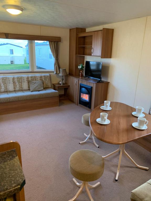 新罗姆尼Cosy Private Caravan Romney Sands Holiday Park的客厅配有桌椅和壁炉