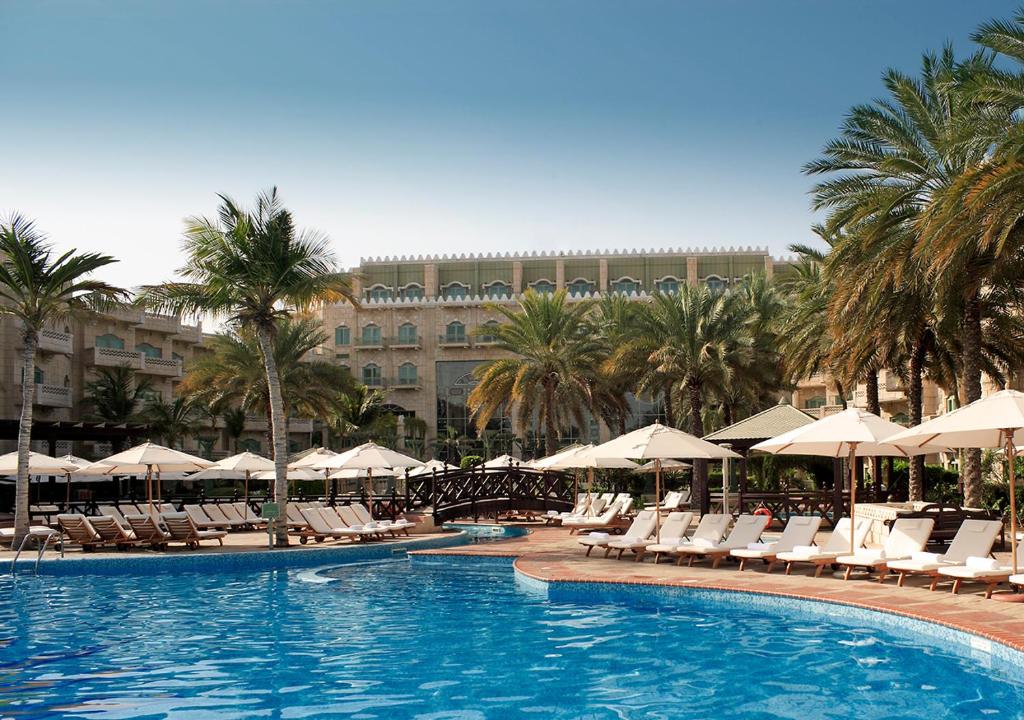 马斯喀特凯悦大酒店马斯喀特的一个带椅子和遮阳伞的游泳池和一座建筑