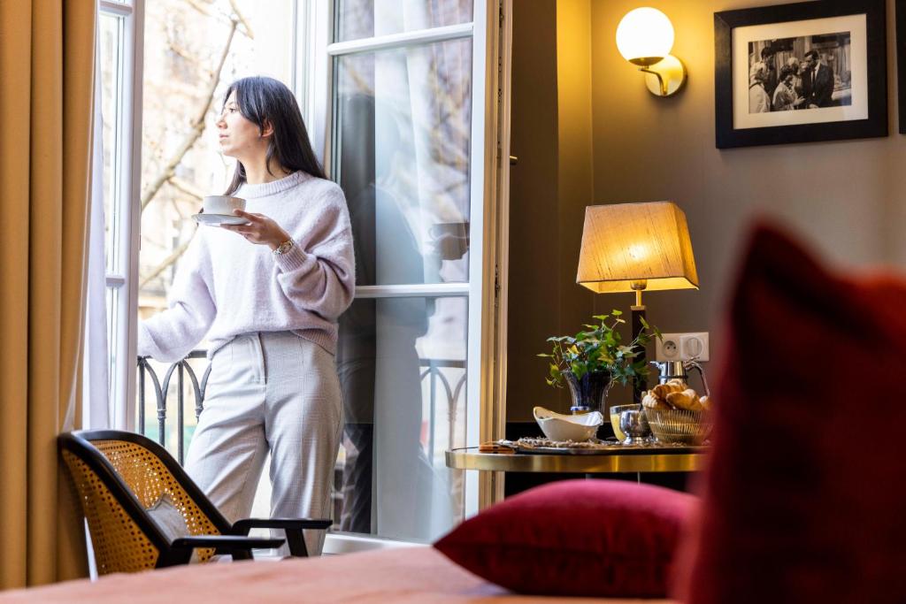 巴黎迎宾酒店的站在窗户外拿着咖啡的妇女