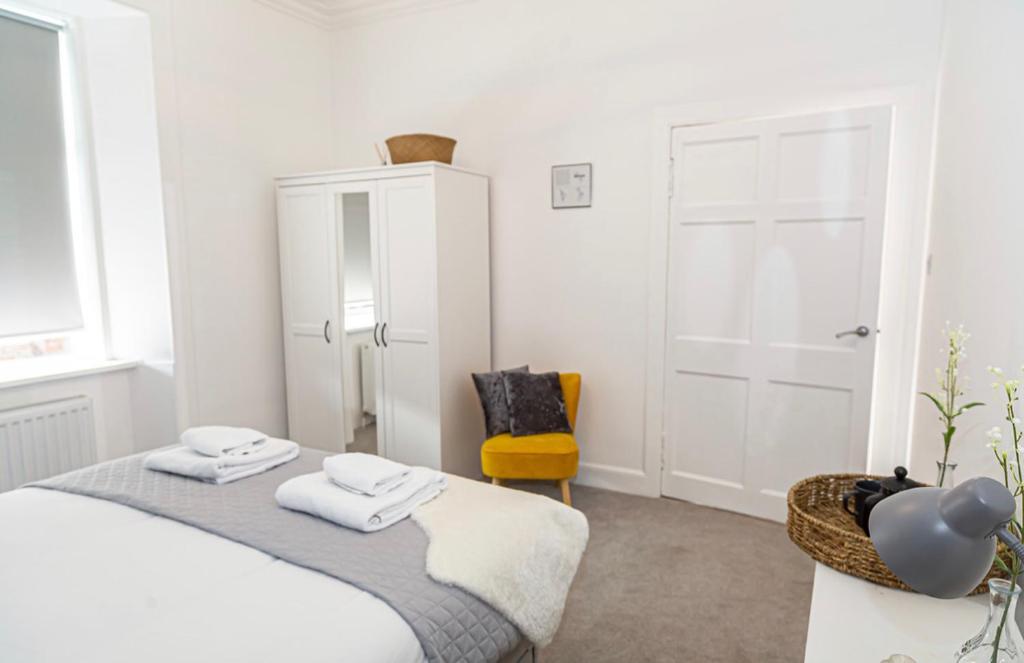 艾尔The Mila - Ayr Racecourse - Coorie Doon Apartments的白色卧室,配有床和黄色椅子