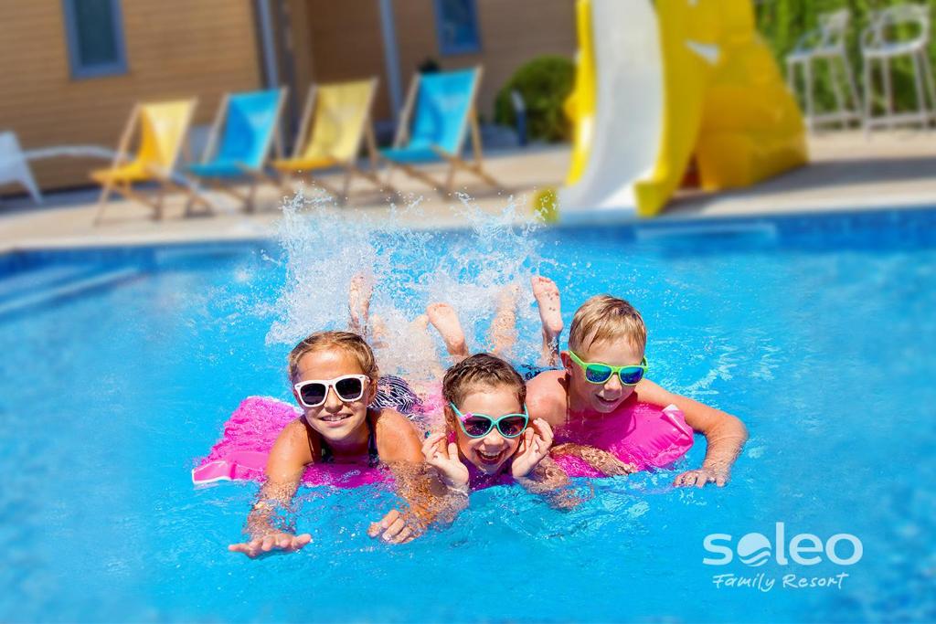 里沃SOLEO Family Resort的三个孩子穿着太阳镜在游泳池里